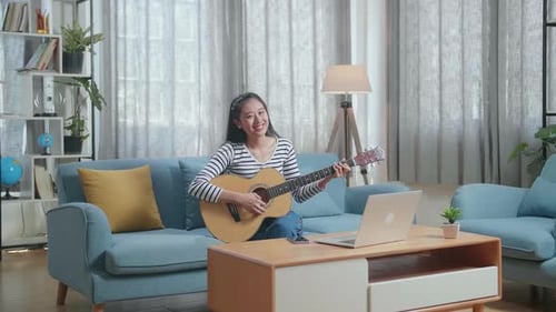 Young Woman Plays Guitar and Smiles at Home