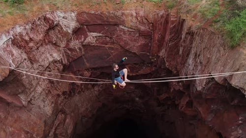 Man Tightrope Walking Over Rocky Pit in Wilderness