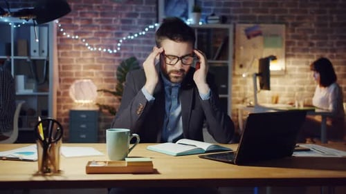 Stressed Guy Using Laptop Then Touching Head Feeling Headache in Dark Office