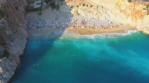 People Swim on Light Blue Sea in the White Sandy Beach Near the Rocky Mountainside