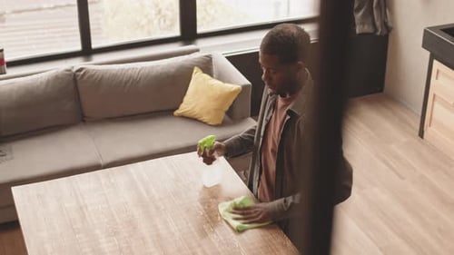 Man Cleans Table in Bright Apartment