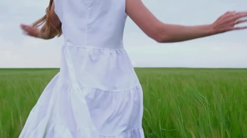 A Young Girl Runs Across a Green Wheat Field in a White Dress