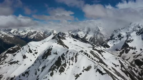 Air Flight Through Mountain Clouds Over Beautiful Snowcapped Peaks of Mountains and Glaciers