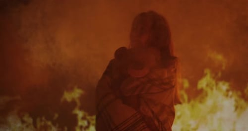 Woman Wrapped in Blanket Stands Before Intense Flames