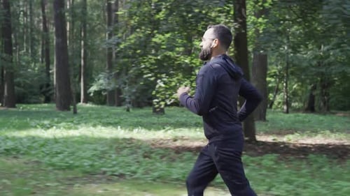Adult Man Running Through Summer Forest Camera Following Runner in Wireless Headphones Healthy