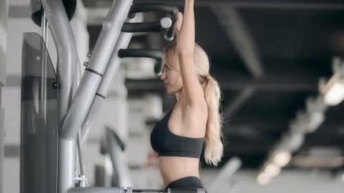 Sport Woman Doing Pulling Up Exercise on Fitness Machine in Modern Gym