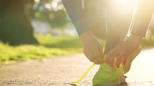 Frau bindet Schnürsenkel beim Joggen oder Spazierengehen bei Sonnenuntergang