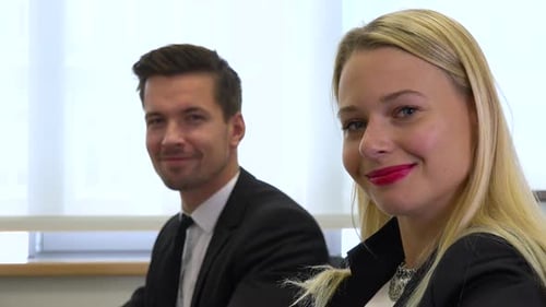 Two office workers, man and woman, work on computers and smile at the camera - closeup
