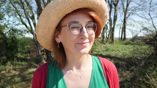 Smiling redheaded woman wearing straw hat looking at camera