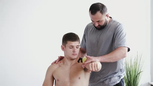 Physiotherapist Placing Kinesiology Tape on Shoulder of Athlete in Clinic