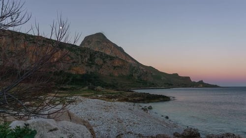 Timelapse of twilight to golden sunrise with moon setting behind mountain of Monte Cofano at mediter