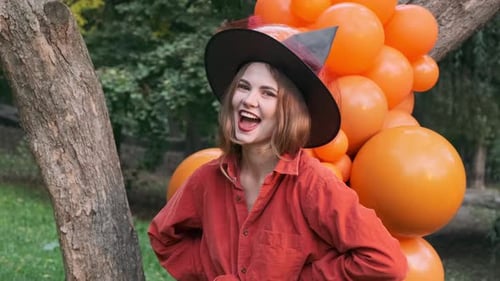 Young Woman in Witch Hat Laughing with Balloons