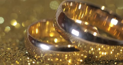 Gold Wedding Bands Intertwined on Glittering Gold Surface