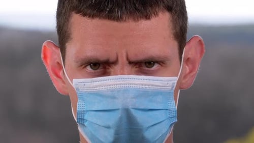 Young Man in a Medical Protective Face Mask Looking at the Camera on the Street Background