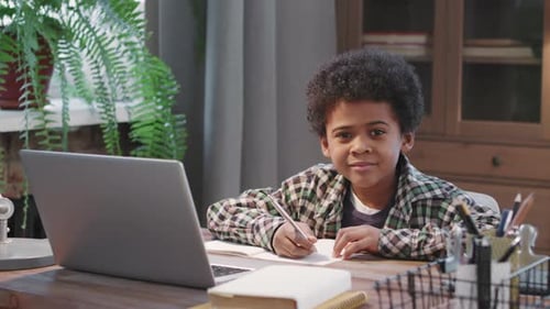 Boy Studies at Home with Laptop and Notebook