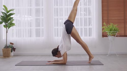 Posture de yoga debout, Vrischikasana sur tapis, femme asiatique en tenue de sport s'entraînant à l'intérieur.