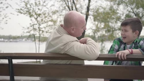 Grandfather and Grandson Sitting in the Park Near the River on the Bench