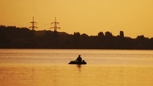 Silhouette of a man floating in a boat on the river surface on the background of an evening trees.