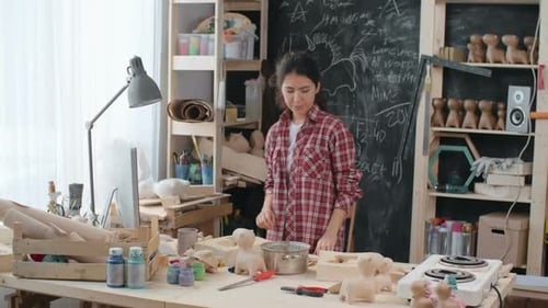 Woman working at cluttered craft workshop, putting on apron