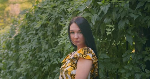 Young and beautiful woman in the park on the background of green leaves