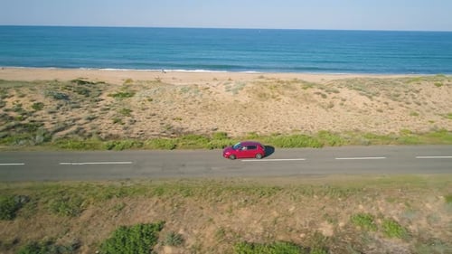 Red Car Driving Slowly on Coastal Asphalt Road Along the Black Sea Shore