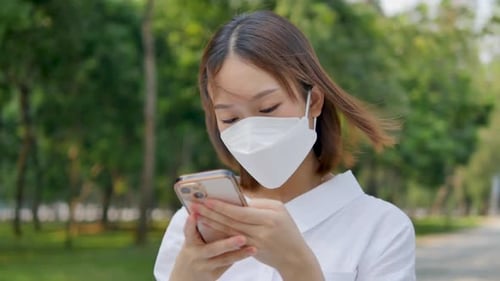 Woman Walking in Park Looking at Her Phone