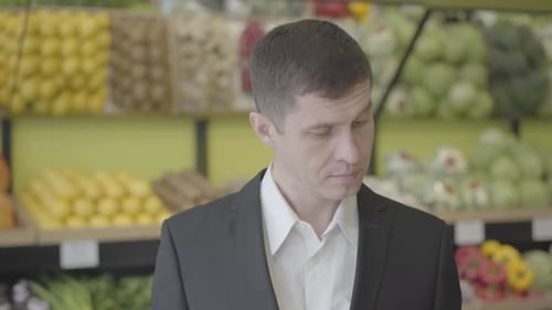 Close-up Portrait of Serious Caucasian Man Choosing Pear in Grocery Shop. Handsome Guy Smelling