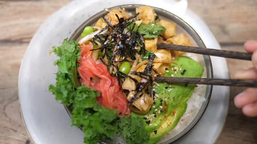 Top View of Chopsticks Picking a Piece of Tofu From Vegan Poke Bowls with Seaweed Watermelon Radish
