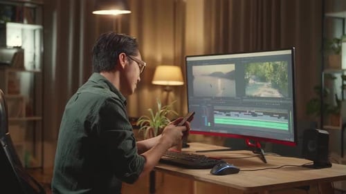 Editor de Vídeo Masculino Asiático Trabaja Y Usa El Teléfono Móvil Con Su Ordenador Personal