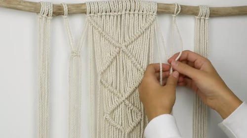Uma mulher tece com as próprias mãos um padrão de fios de macramê para decoração ou decoração de casa.