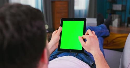 Student Boy Resting on a Couch Using with Green Mockup Screen Tablet Computerin Vertical Portrait