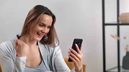 Woman Using Phone Celebrates Good News Indoors