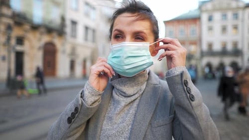 Woman Puts on Face Mask in City Street