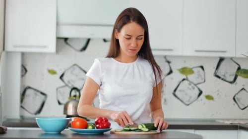 Woman Slicing Cucumber for Salad in Bright Kitchen