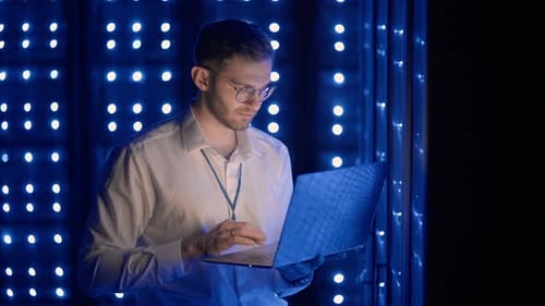 Man Working on Laptop in Blue Server Room