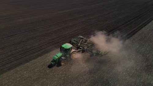 Tractor with harrow system plowing ground on cultivated farm field, agriculture.