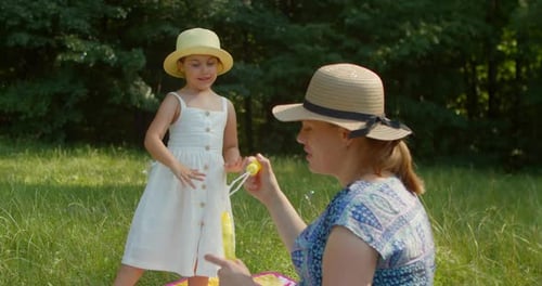 Mother and Daughter Blow Soap Bubbles in the Park