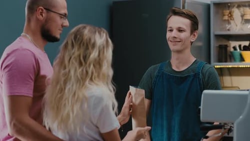 Smiling barista in a coffee shop selling coffee beans in craft bag for customers