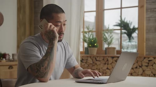 Man Working at Laptop with Cell Phone at Home