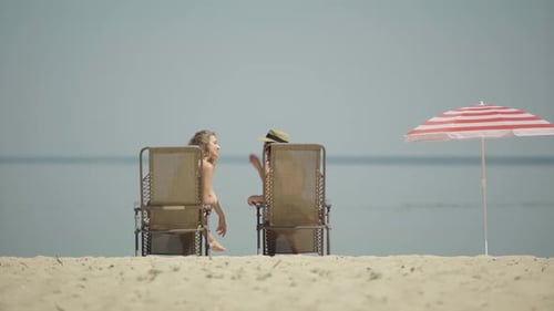Wide Shot Back View of Two Cheerful Caucasian Women Sitting on Sun Loungers and Talking. Happy