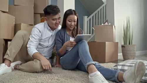 Couple Using Tablet Amidst Moving Boxes in New Home