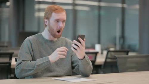 Man at Desk Reacts with Surprise to Smartphone