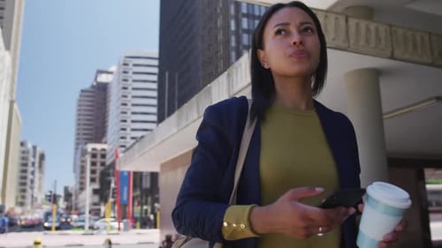 African american woman holding coffee and using smartphone in street