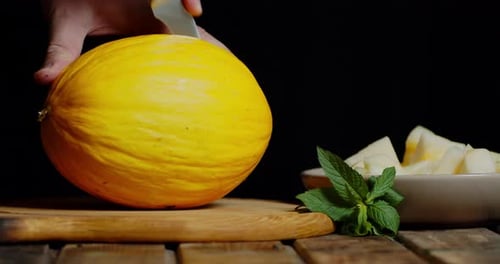 Männliche Hand mit einem Messer schneidet eine frische Melone in zwei Hälften