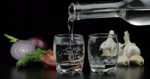 Versez la vodka alcoolisée d'une bouteille dans deux verres à shot. Fond avec des légumes