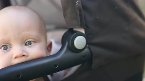 Baby Infant Child Portrait Face in Carriage Licking Plastic Parts of Stroller