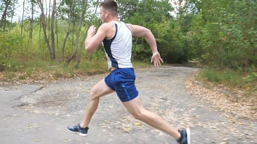 Handsome Strong Sportsman with Wireless Headphones Sprinting Fast Along Trail Near Forest