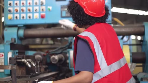 Afroamerikanische Arbeiterin bei Prüfung der Sicherheitsuniform an der Fabrikmaschine