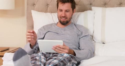 Man Relaxes in Bed with Tablet Computer