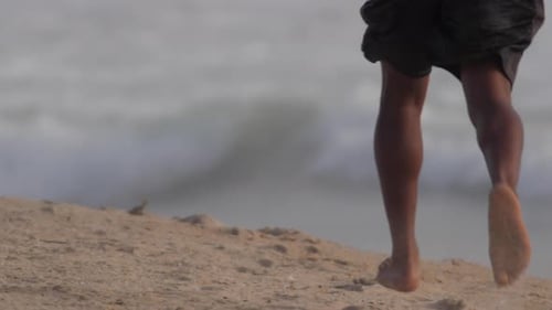 A young mans barefoot feet running on the beach.